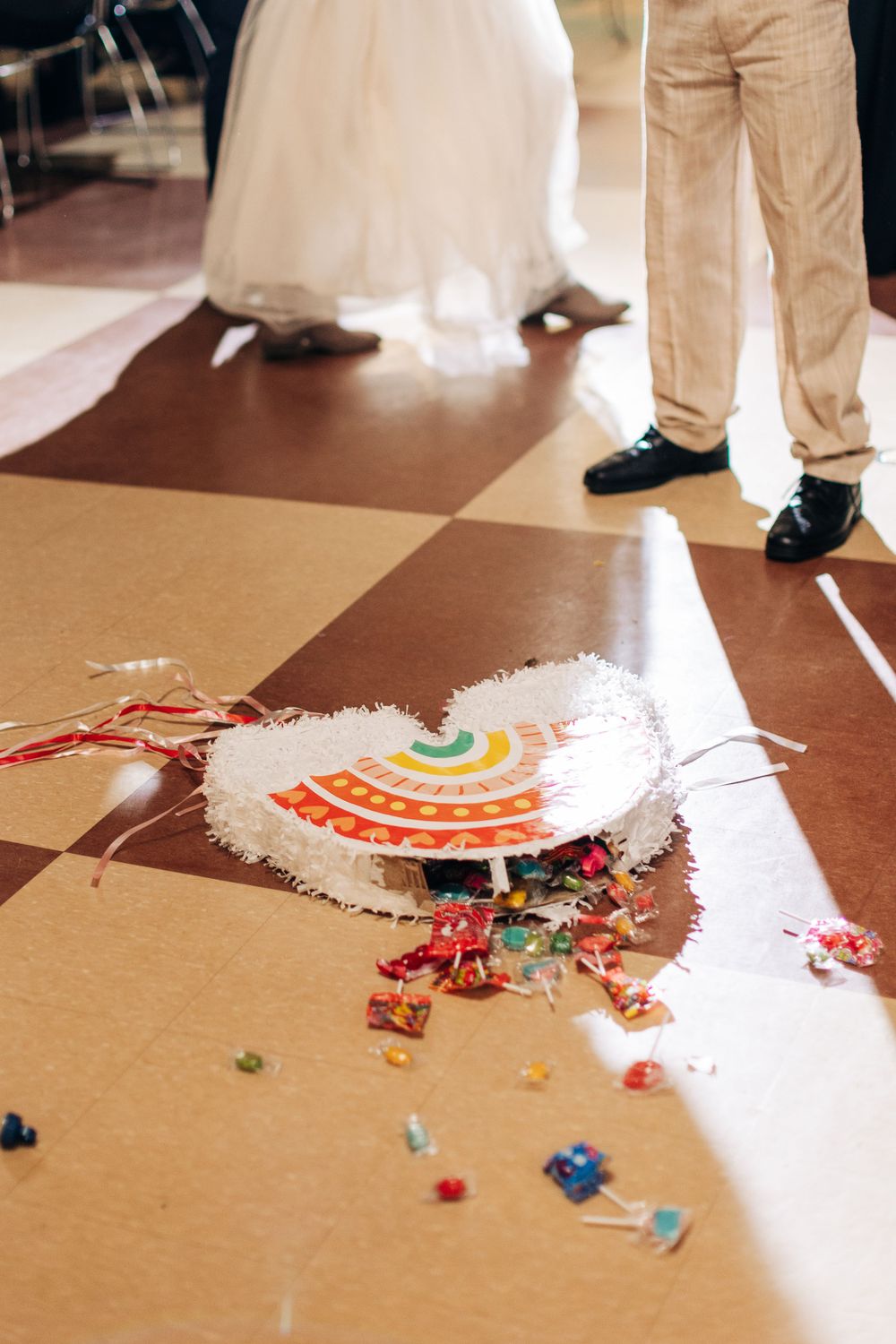 A broken rainbow piñata and scattered candy on a checkered dance floor at an event.
