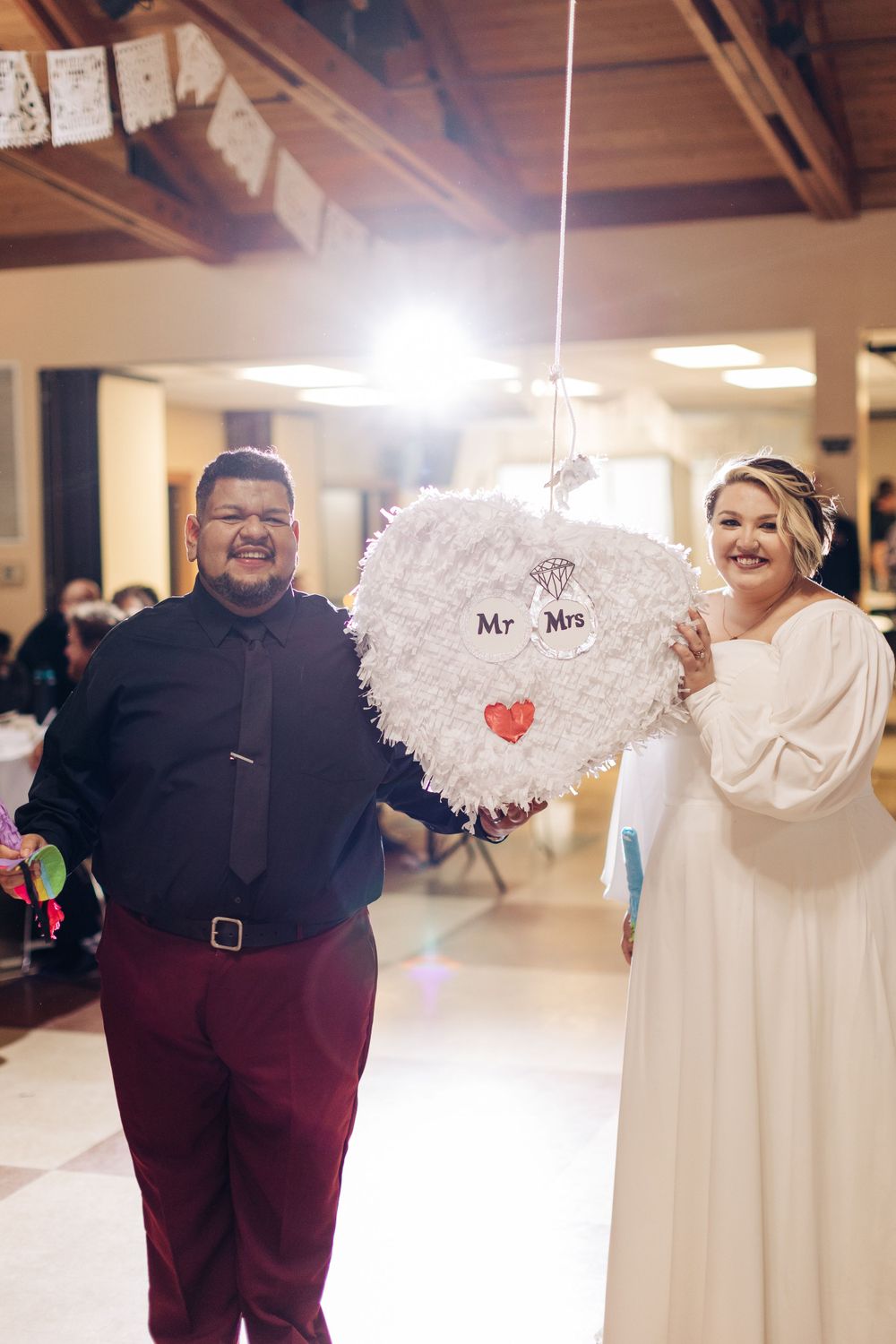 A couple poses with a white decorative 'Mr & Mrs' piñata at their wedding reception.