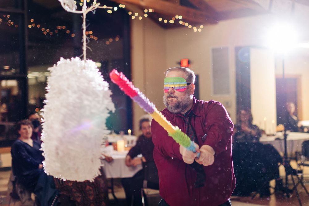 A person in festive attire takes a swing at a hanging white piñata during an indoor party.
