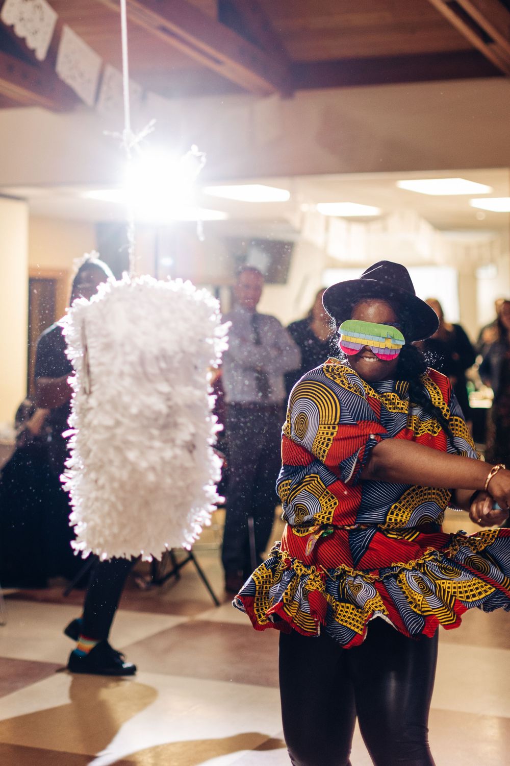 Party guests dance near a white decorative piñata hanging from the ceiling at an indoor celebration.