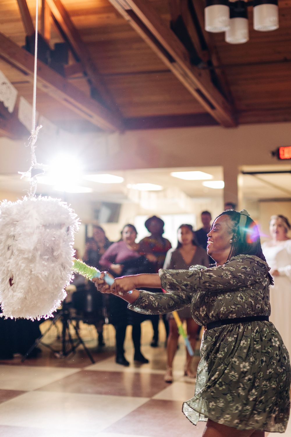 A guest in a patterned dress reaches for a hanging white party decoration at an indoor event.