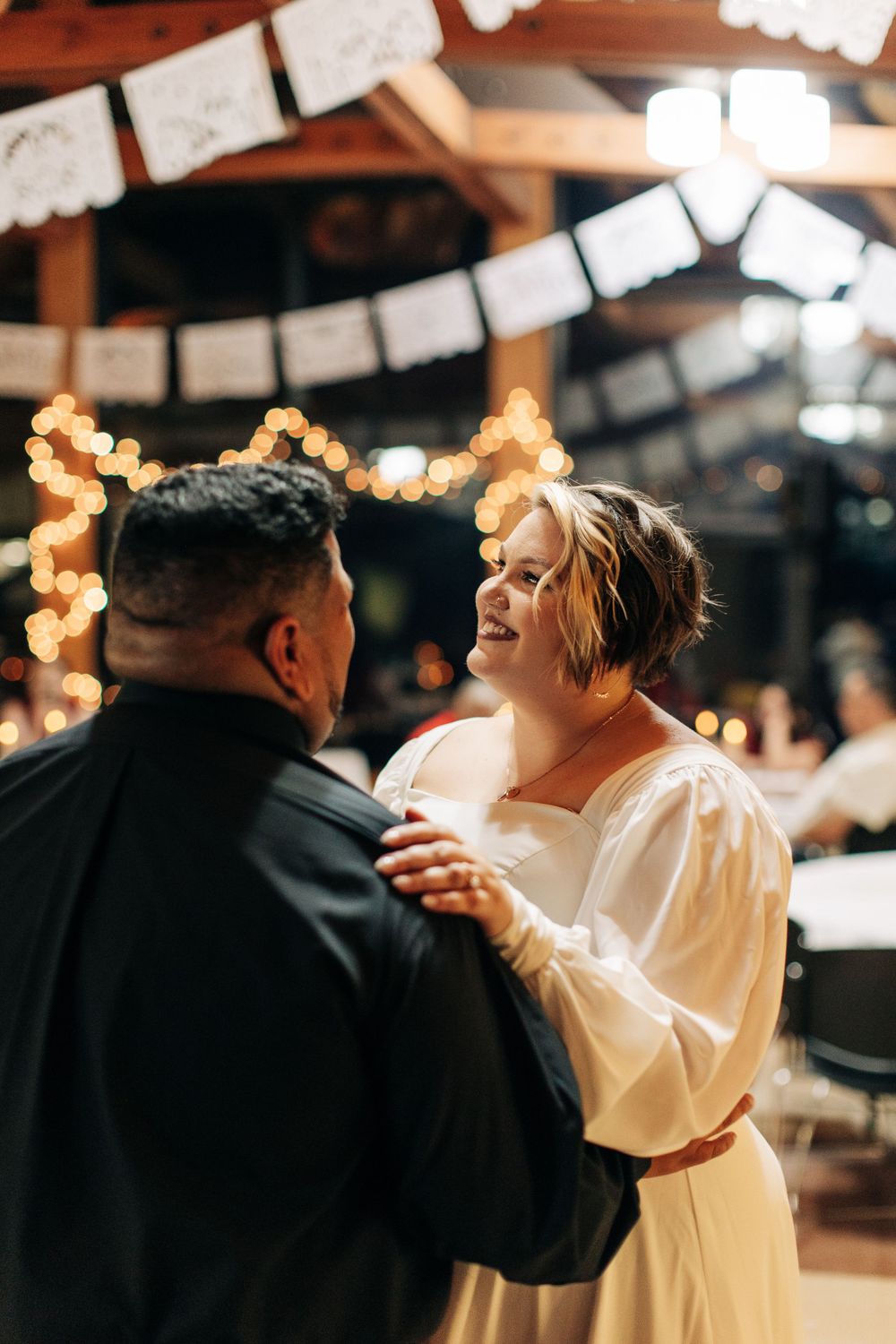 A romantic slow dance moment captured under warm string lights at an indoor celebration.