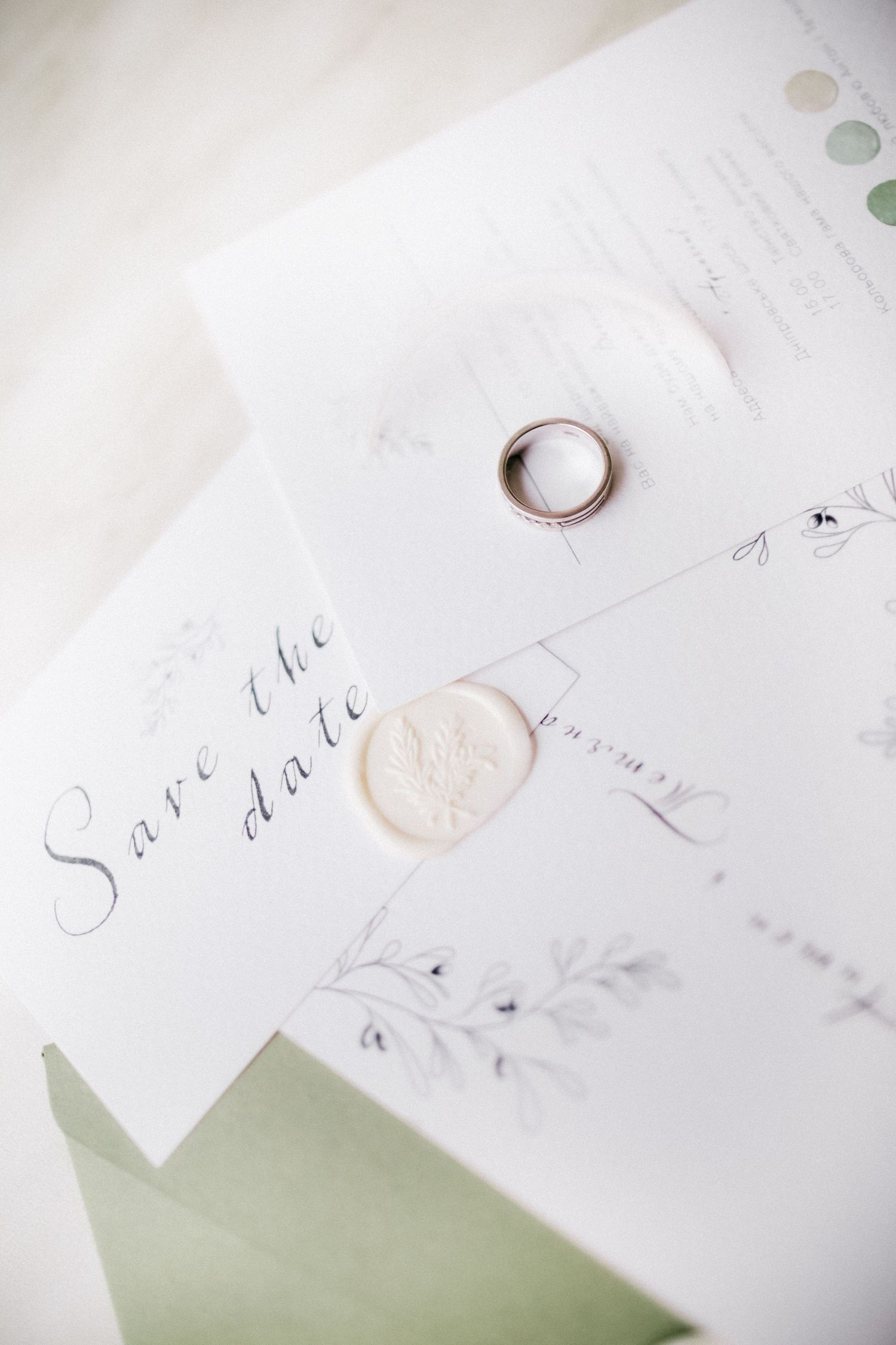 Wedding invitation with wax seal and ring on white paper with sage green accents.