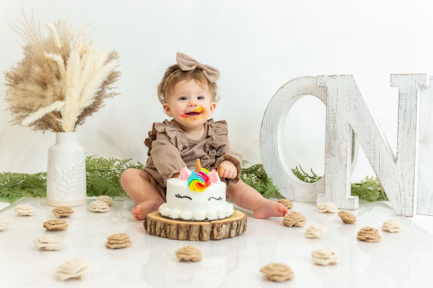 Cake smash photo session features small child in brown outfit with white decorative letter and pampas grass decor.