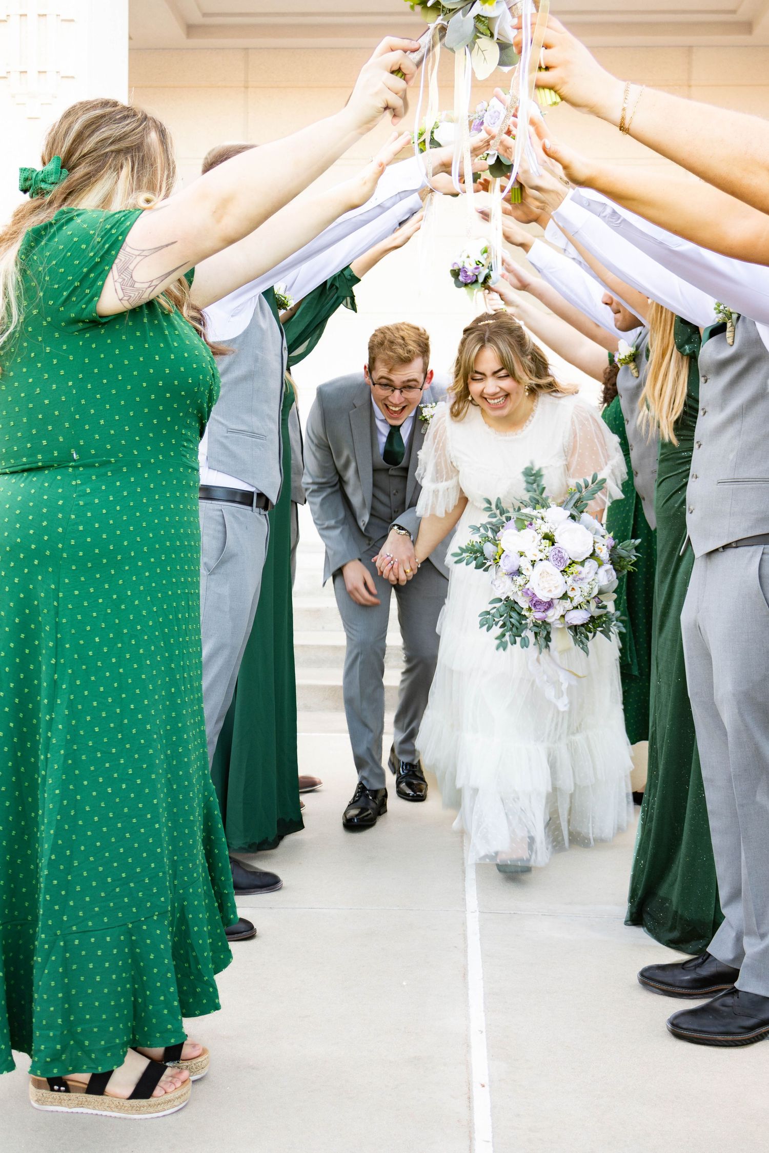 Wedding guests form an archway tunnel with raised arms as a couple walks beneath in a celebratory moment.
