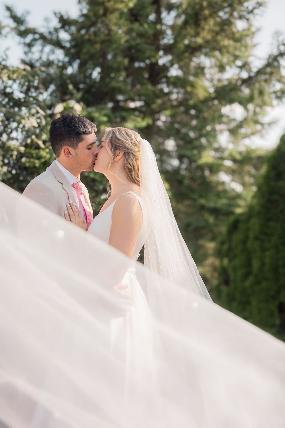 A romantic wedding moment captured outdoors with flowing white veil in the breeze.