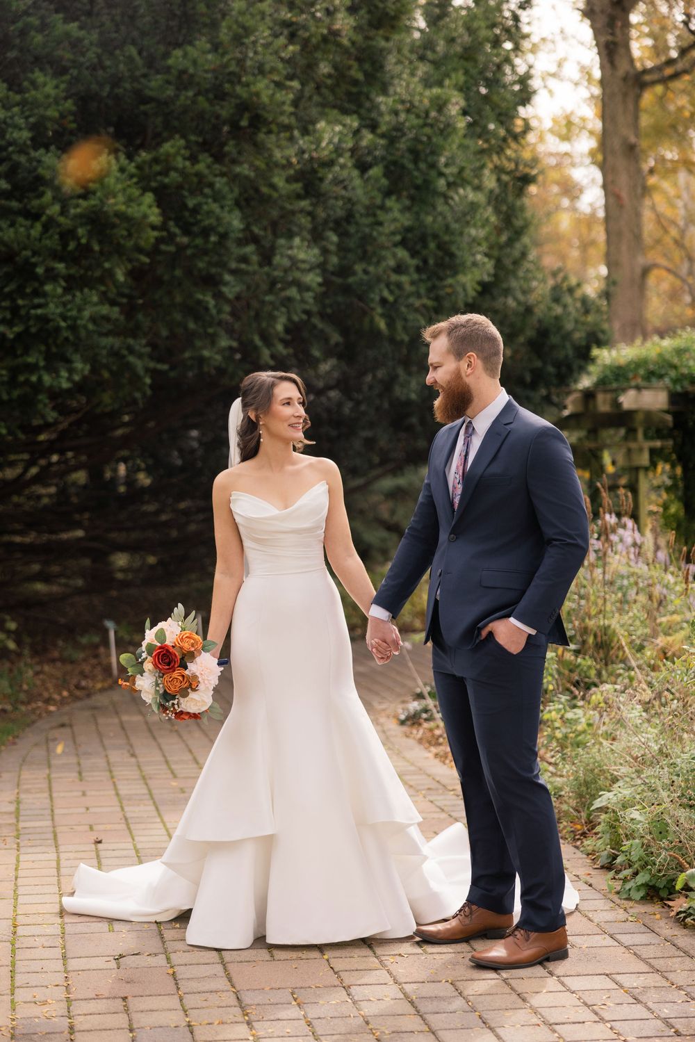 A couple shares a joyful moment on a brick path surrounded by lush garden greenery during their wedding celebration. Columbus, OH Wedding.