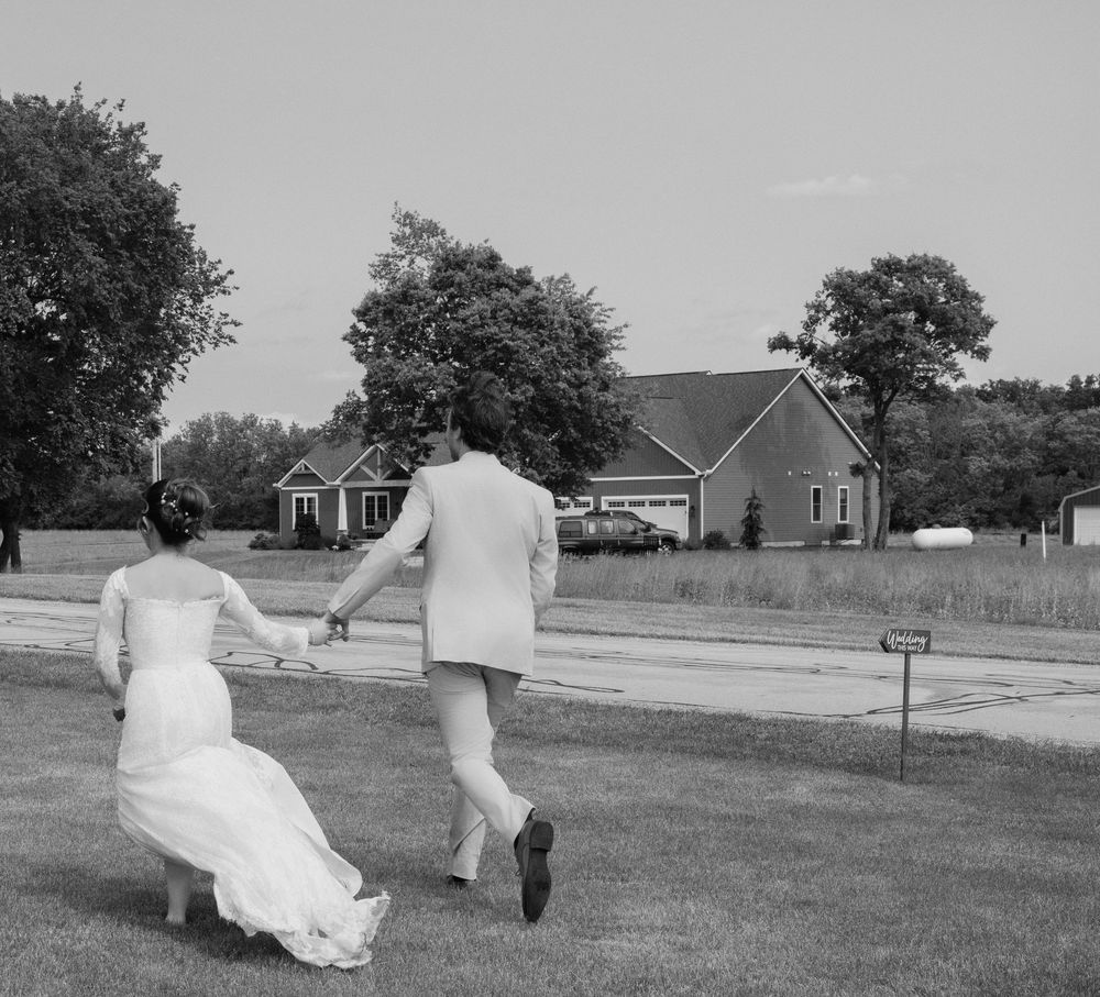 A couple runs playfully across a lawn in wedding attire with houses in the background. Columbus, OH Wedding.