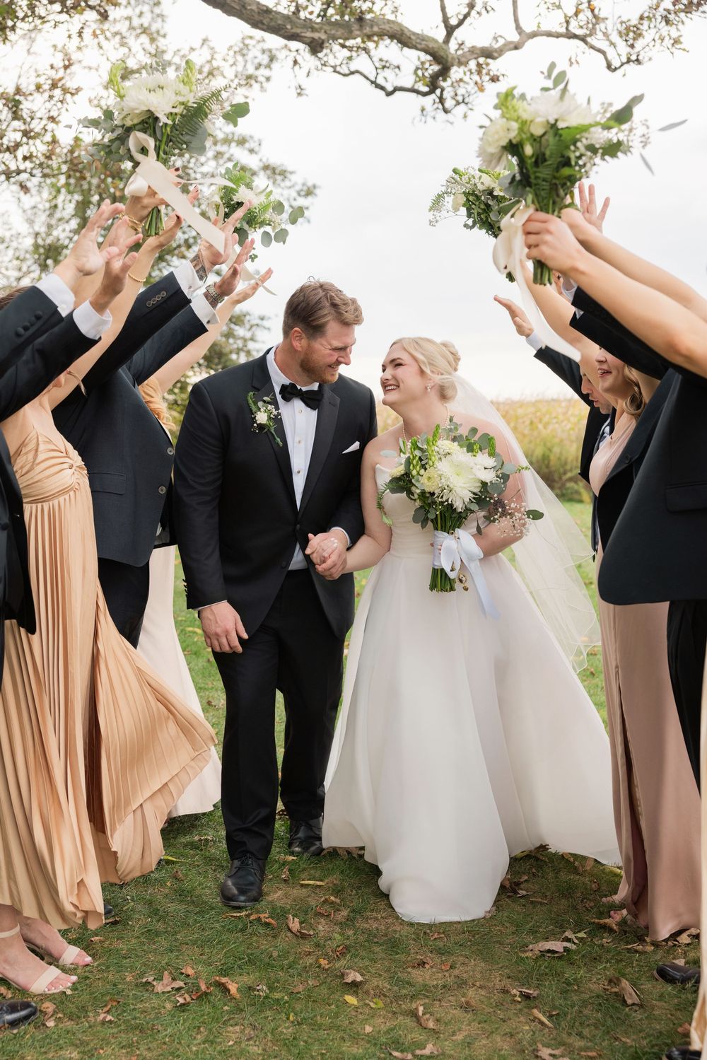 Wedding party in black suits and blush dresses poses playfully under trees during outdoor celebration. Ostrander, Ohio.  Aspen and Alston.
