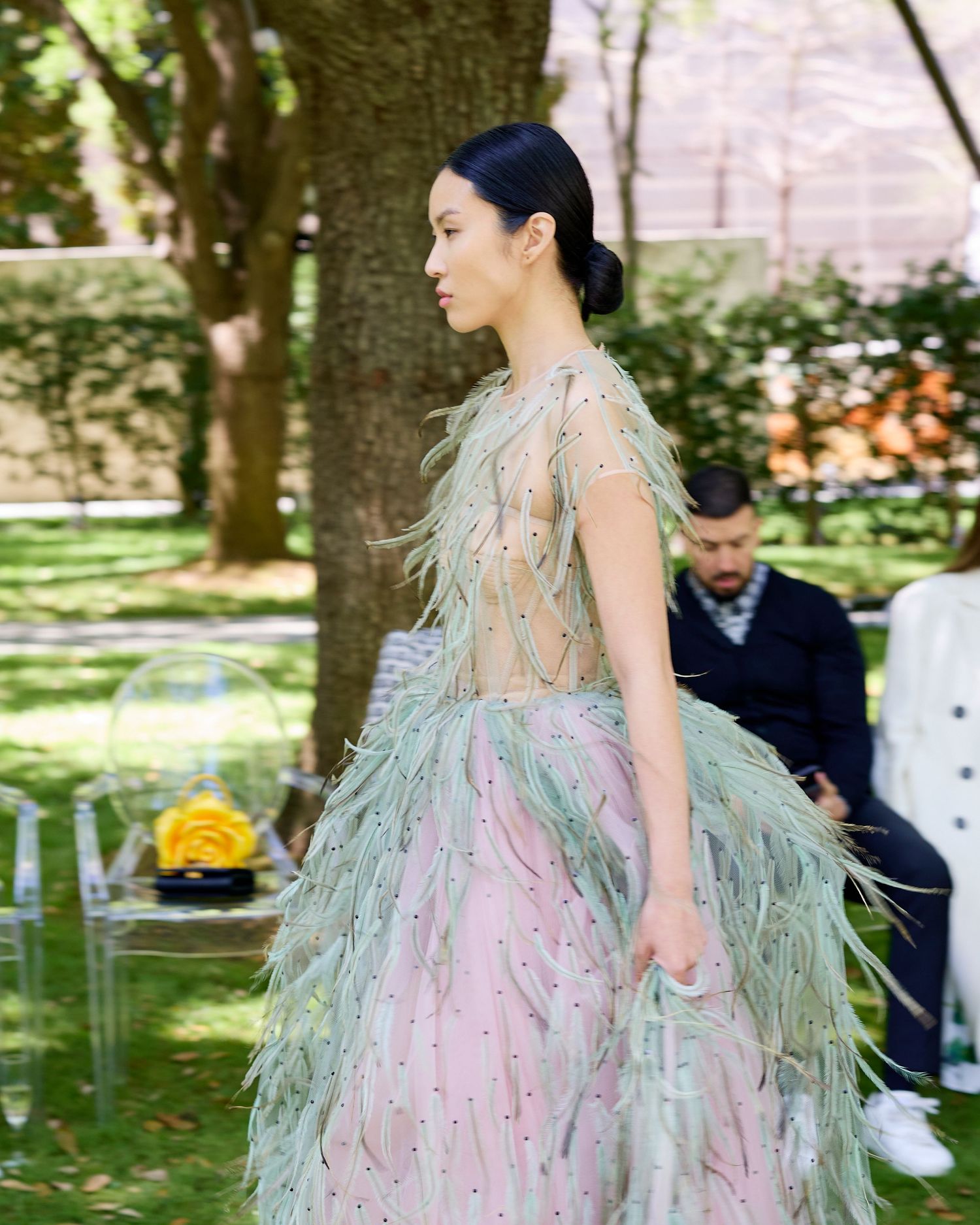An ethereal feathered gown in mint green and pink tones is showcased at an outdoor fashion event.