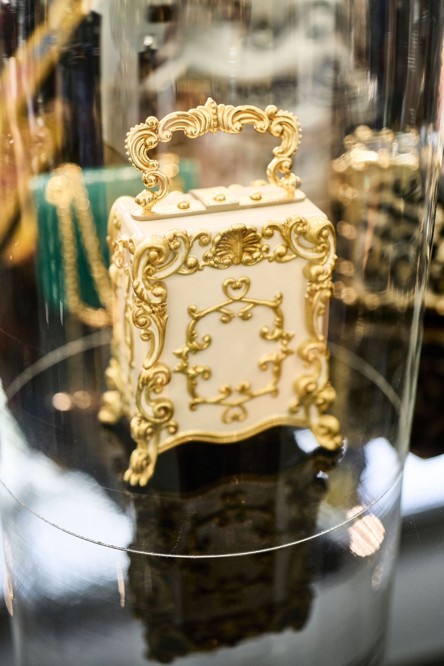 Ornate vintage-style perfume bottle with gold filigree details displayed in glass case.
