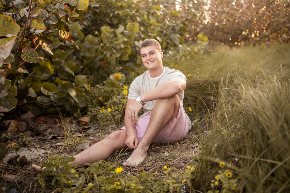 Senior graduation boy sitting in greenery grass at the beach sunset photoshoot session Melbourne Cocoa Beach Vero Florida Brevard County
