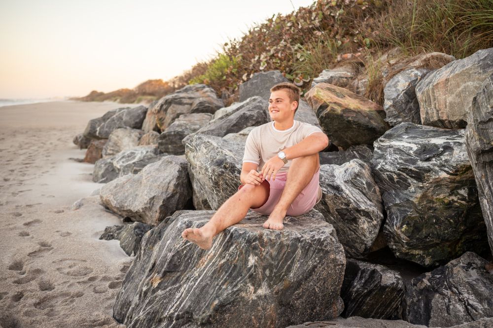 Senior graduation boy sitting on rocks at the beach sunset photoshoot session Melbourne Cocoa Beach Vero Florida Brevard County