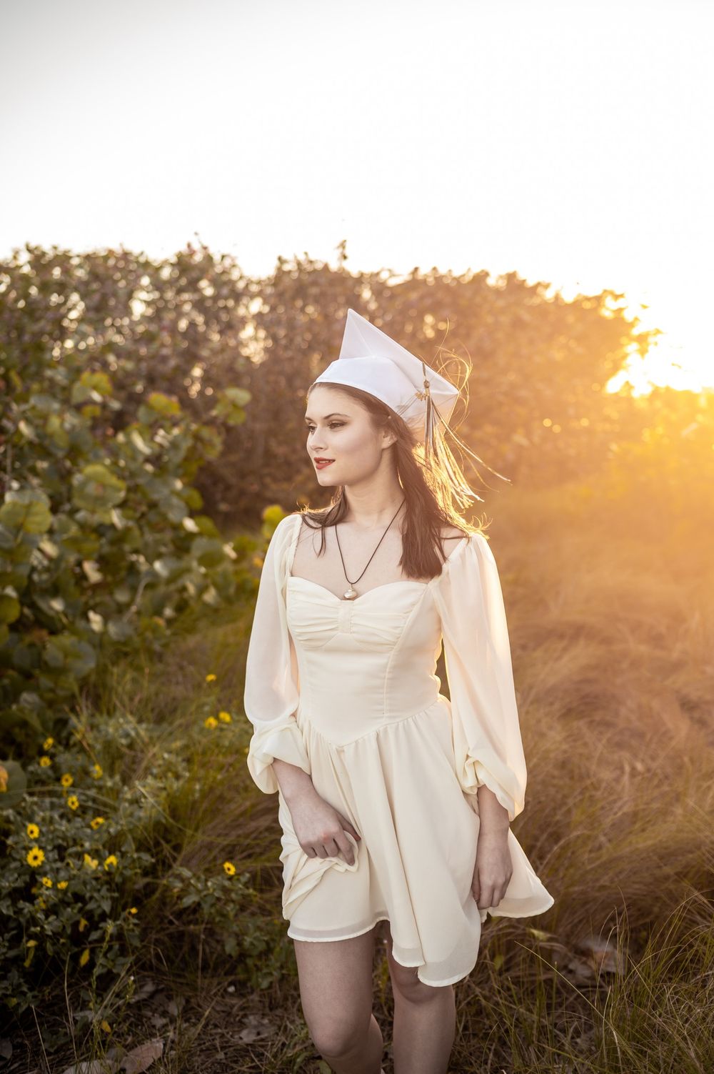 Beautiful senior girl with graduation cap and dress in the greenery at sunset field Satellite Beach Florida Brevard County Senior Photoshoot