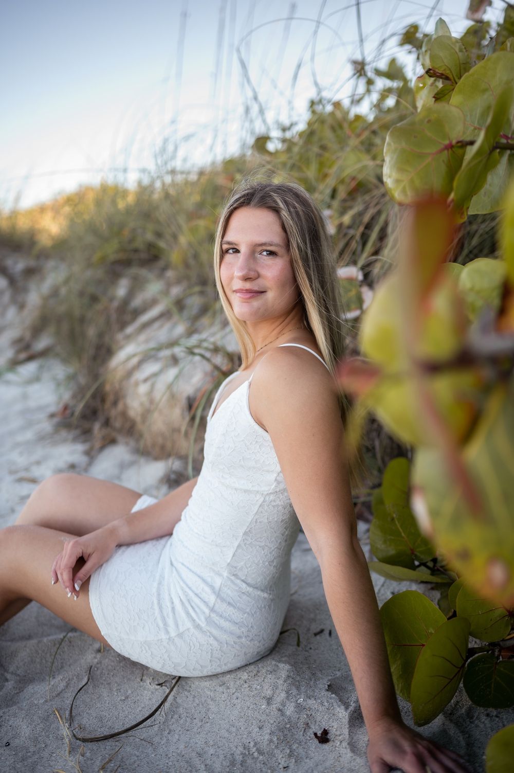 Senior girl graduation photoshoot session in white dress sitting in sand at beach sunset Melbourne Cocoa Vero Florida Brevard County