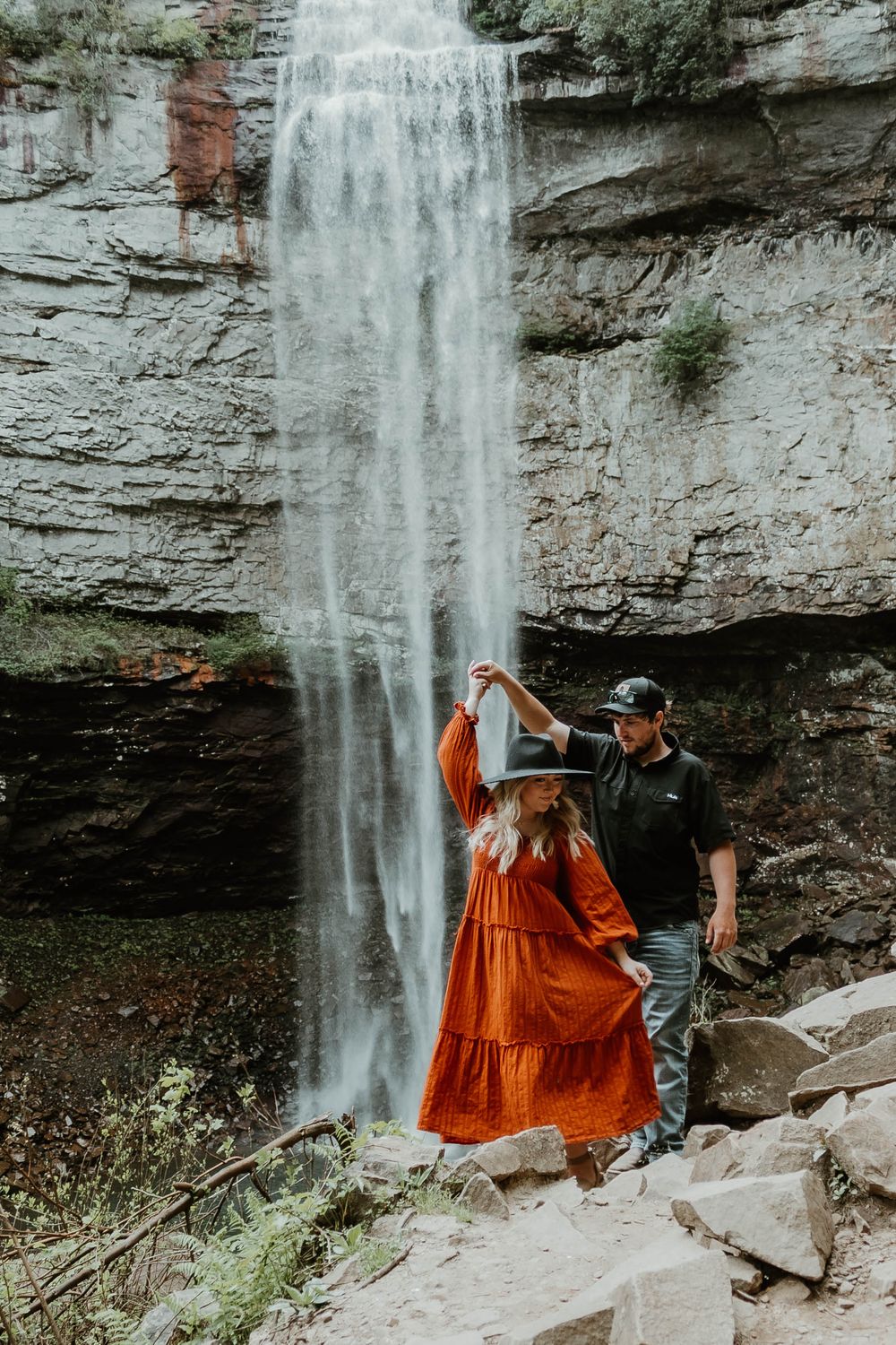 Couple enjoying a romantic moment by a majestic waterfall in a natural setting.