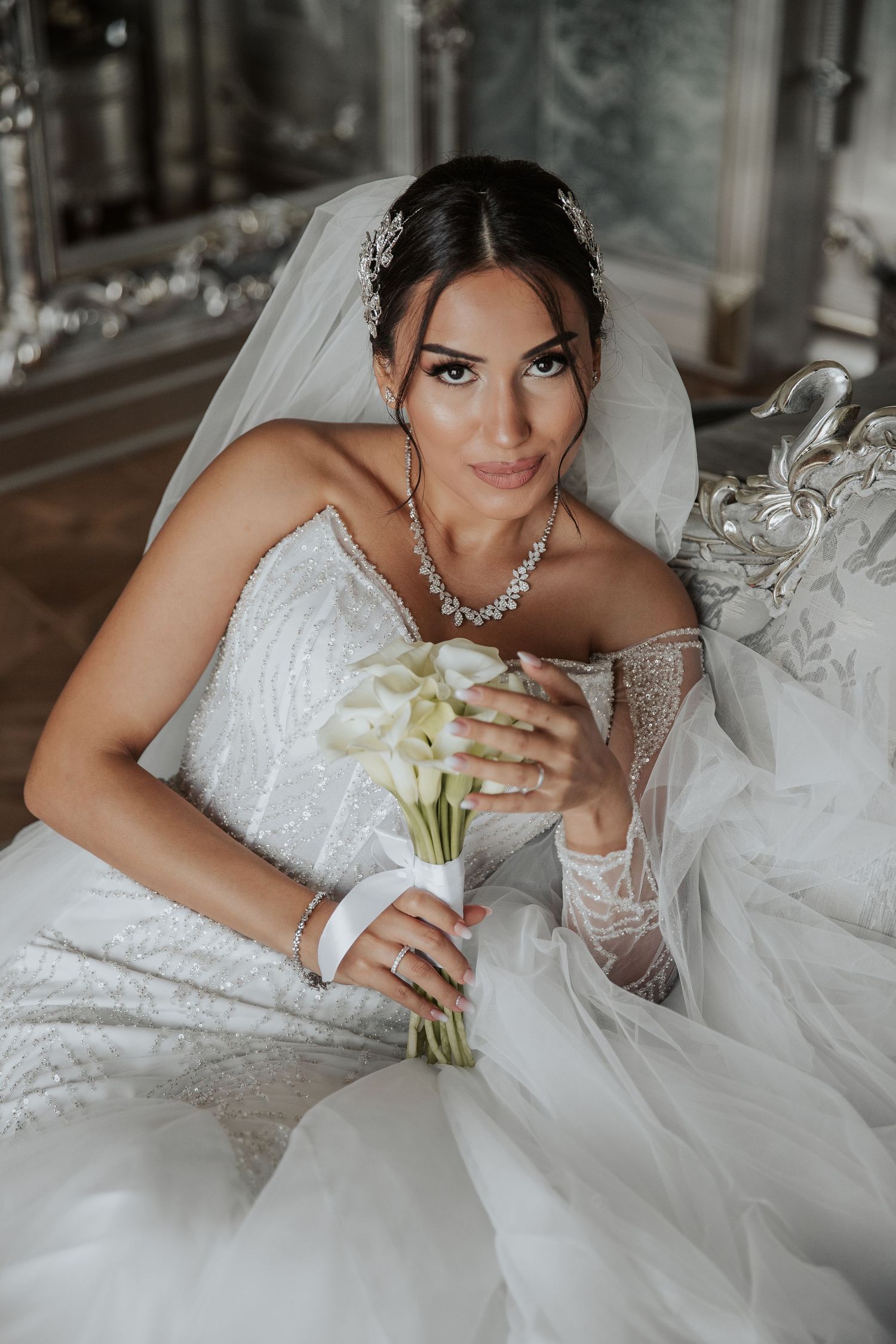 Elegant bride in lace wedding gown holding white calla lily bouquet.