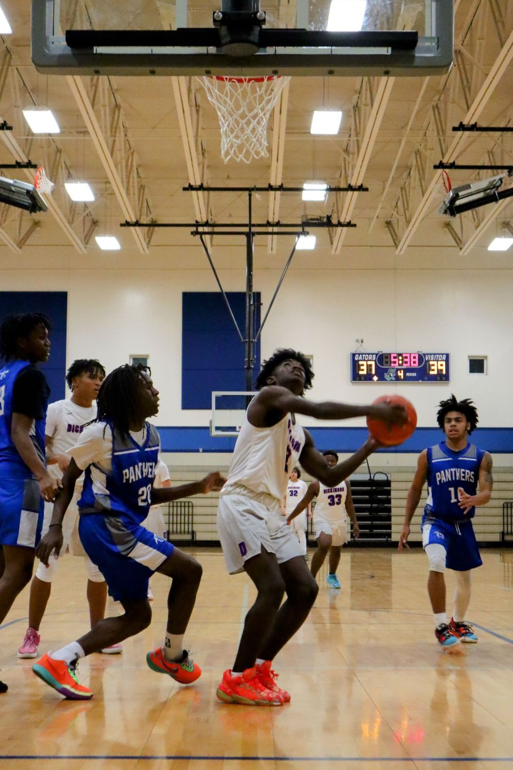 Multiple players dive and stretch for a loose basketball on the gymnasium floor.