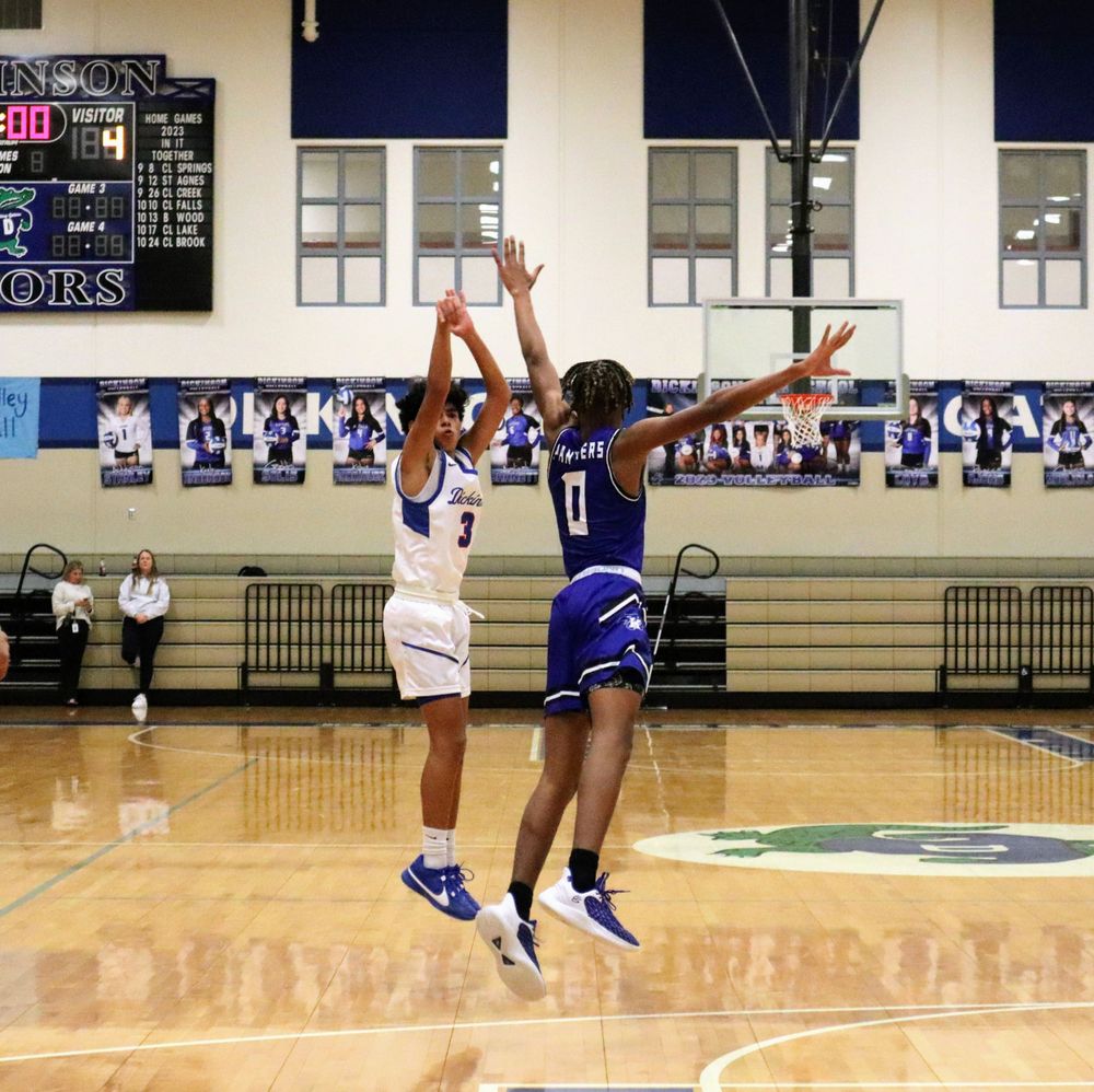 Basketball players jump high competing for the ball near the basket during a game.