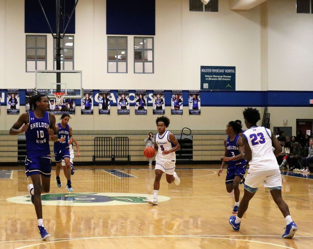 Basketball players in white and blue jerseys compete for ball control during a game.