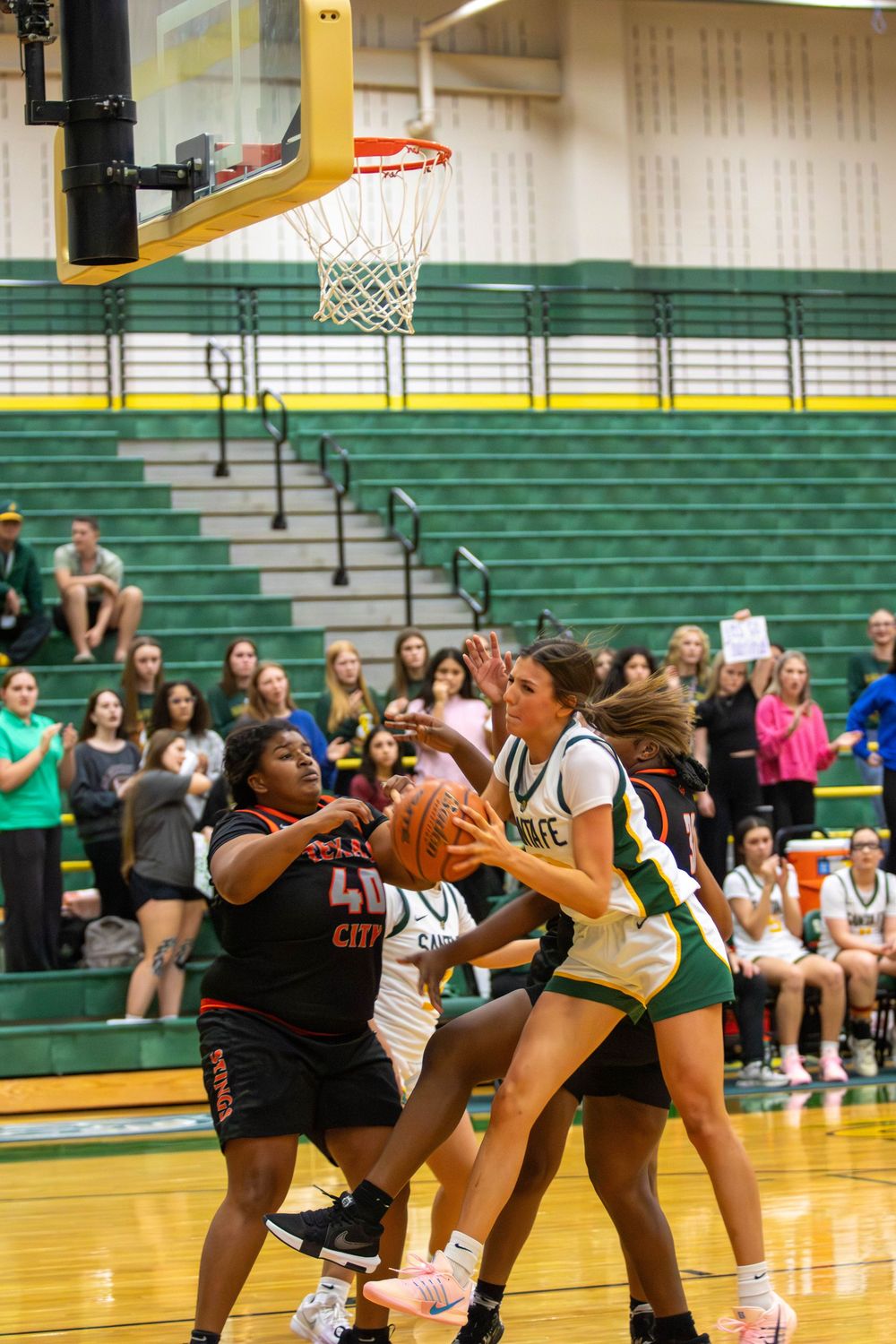 Players battle for rebound under basketball hoop during competitive high school game.