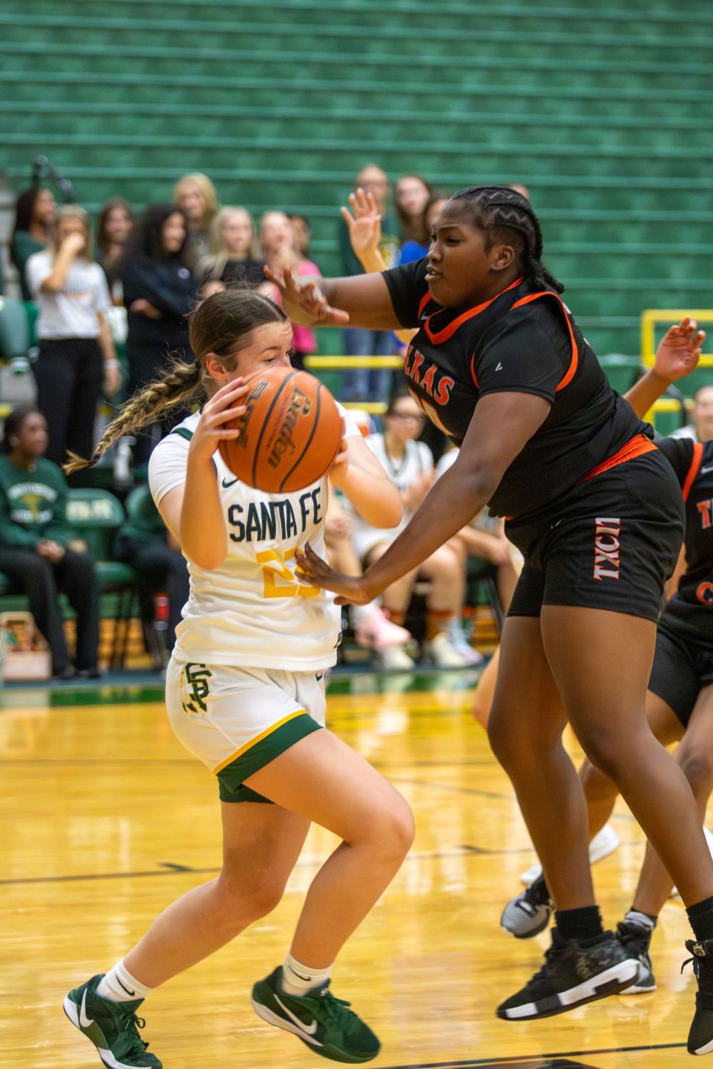Female basketball players competing intensely for the ball during a game on a wooden court.
