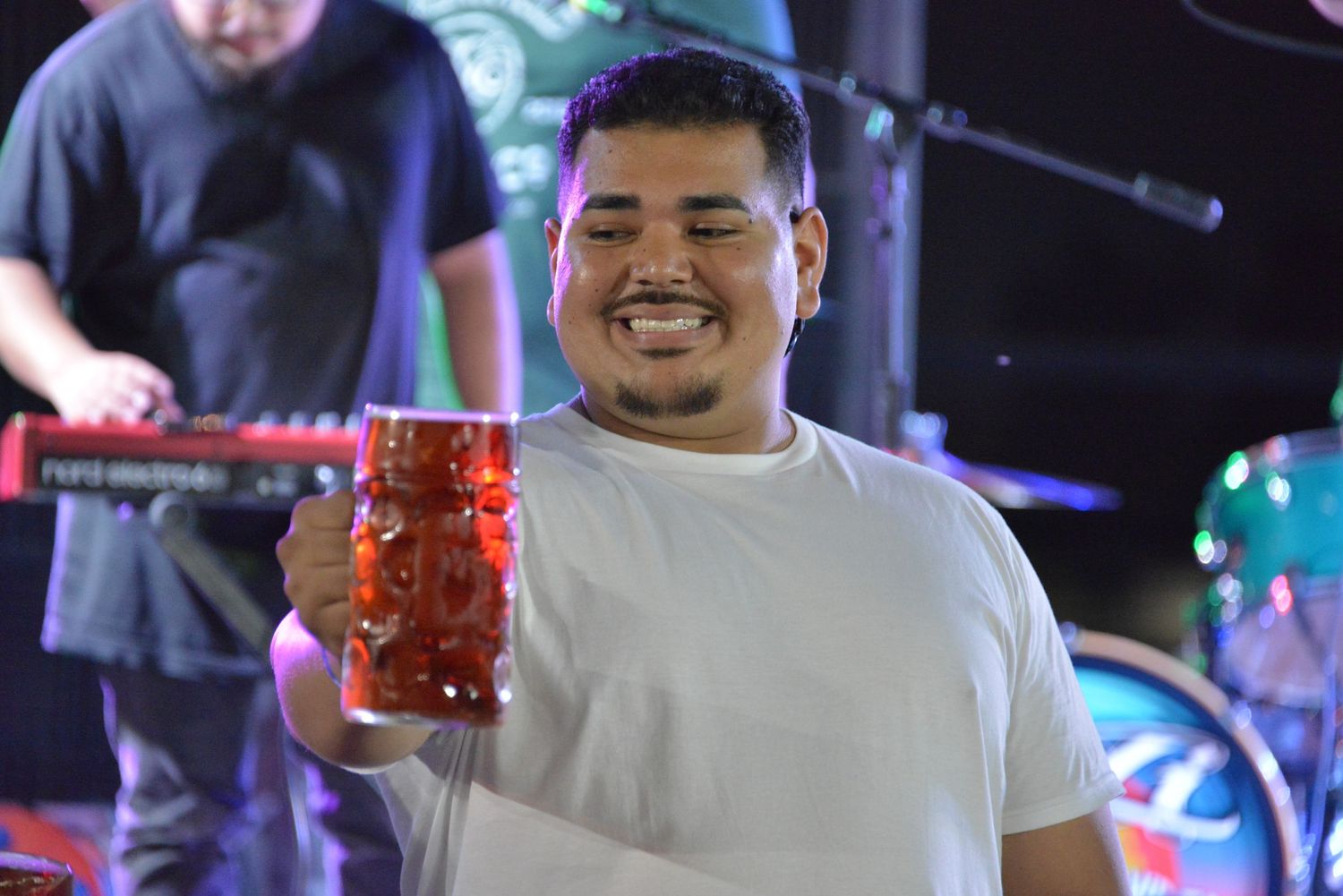 Person enjoying a beer during a live music performance at a nighttime venue.