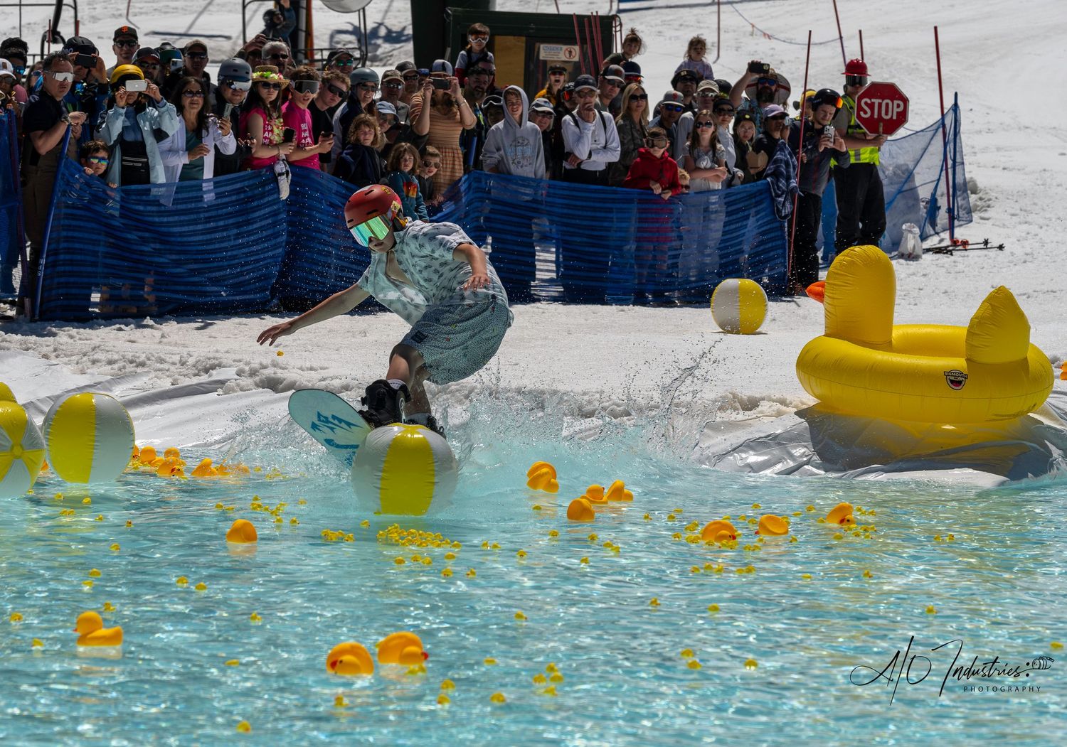 Skier performs trick while crossing water pool during slushy spring skiing event with crowd watching behind barriers.