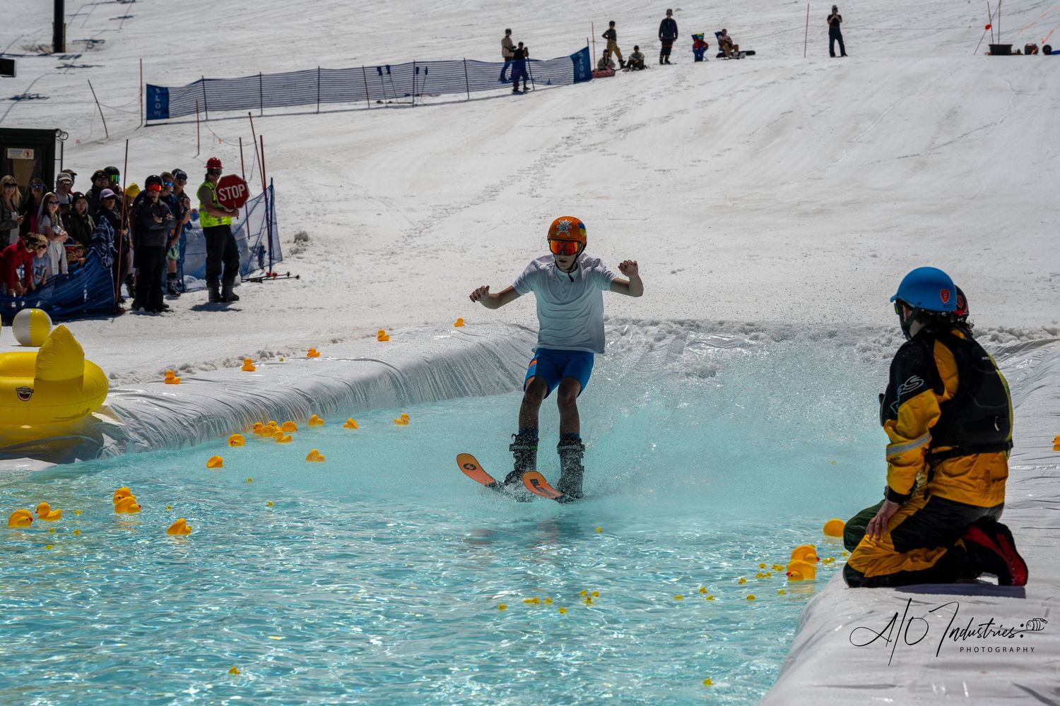 Skier attempts to cross pool of water with yellow rubber ducks during winter resort event.