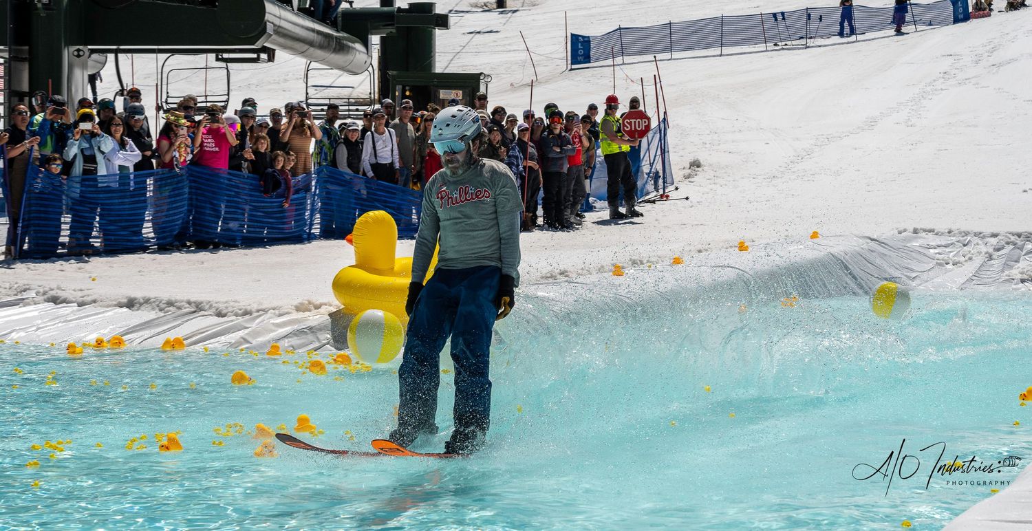 Crowd of spectators watches skier preparing to cross pool during spring skiing event.