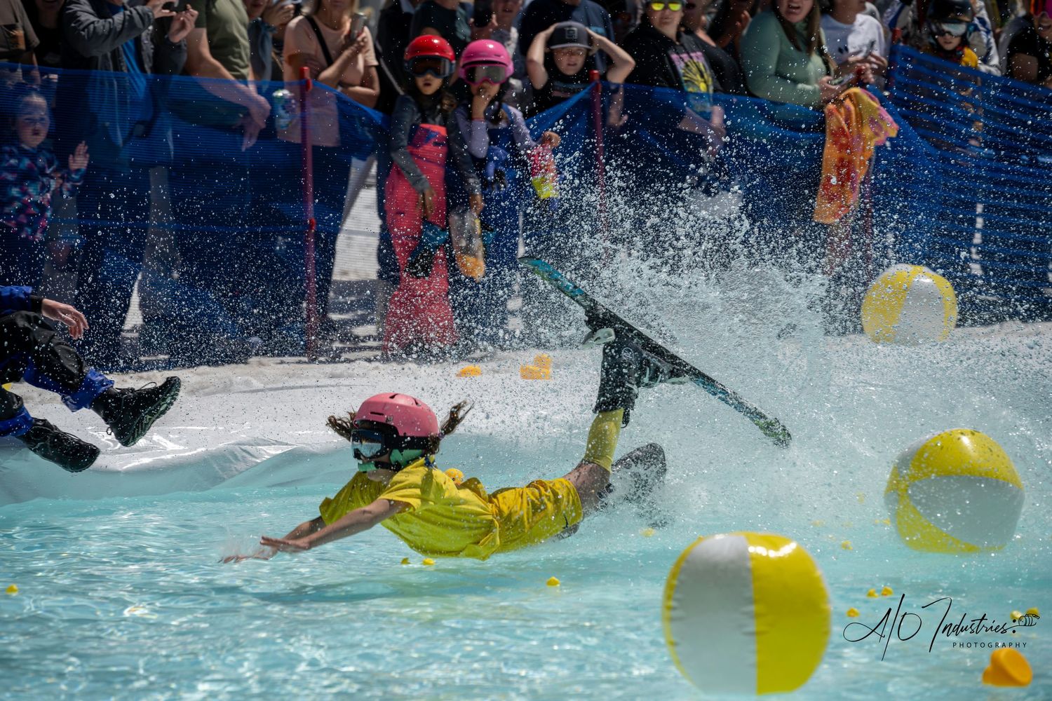 Skier in bright yellow outfit falls dramatically into water during pond skimming competition.