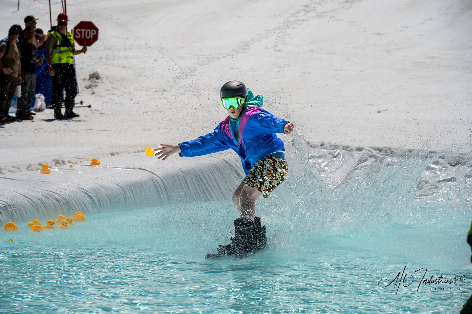 Snowboarder glides across blue water during pond skimming competition.