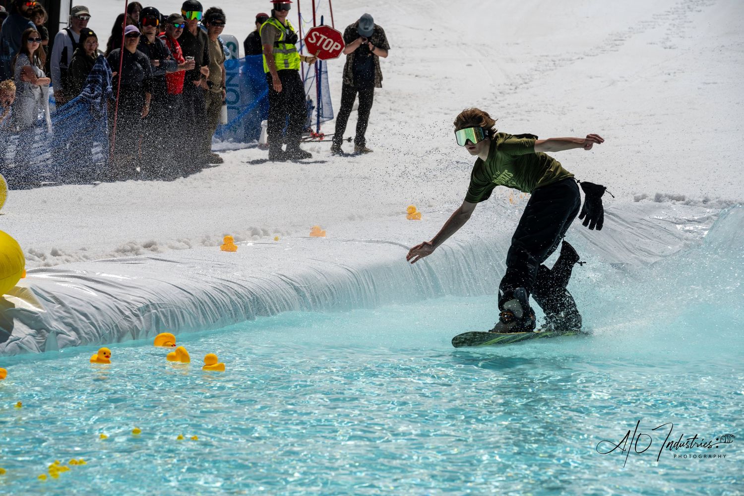 Skilled snowboarder rides across pool of water during pond skimming event.