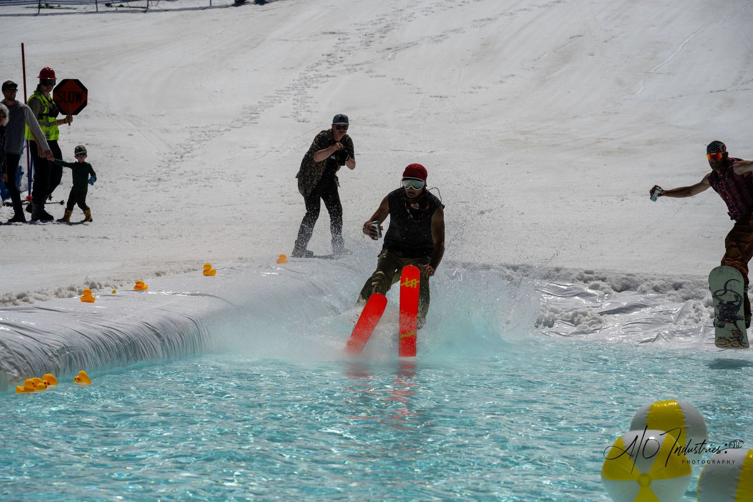 Multiple snowboarders attempt to cross water pool during winter sports event.