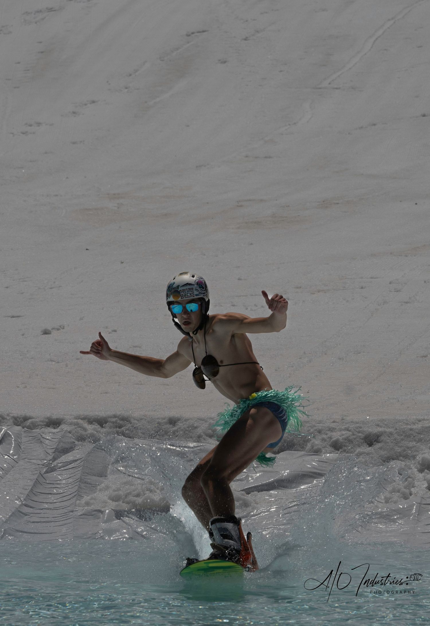 Shirtless snowboarder in tutu performs trick while crossing water pool.