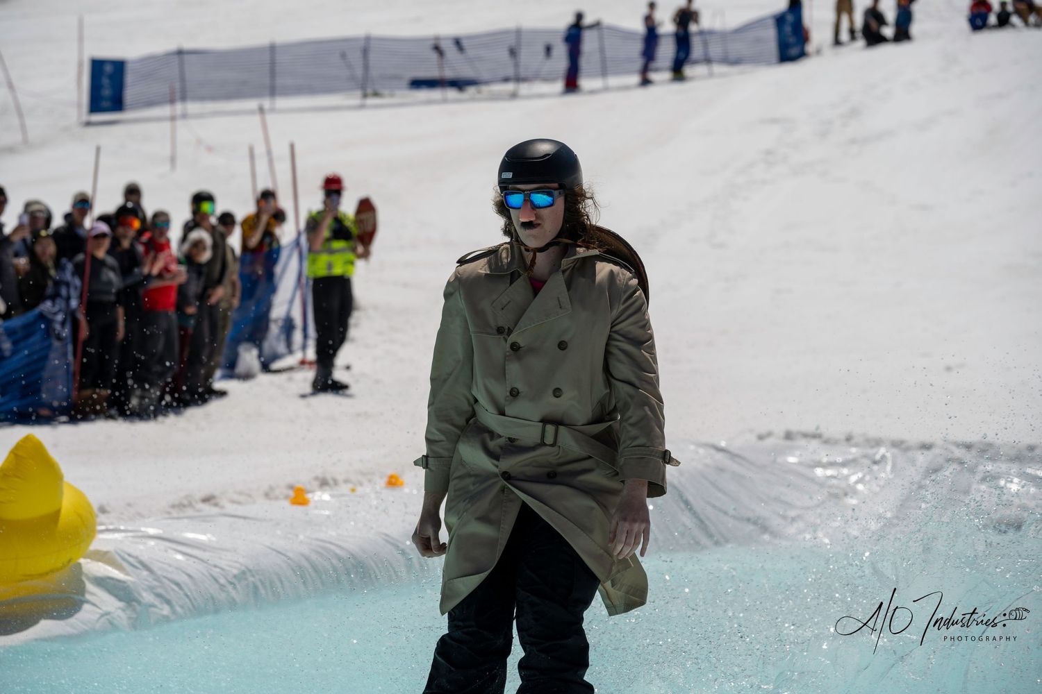 Spectators watch as snowboarder skims across water pool at winter resort event.