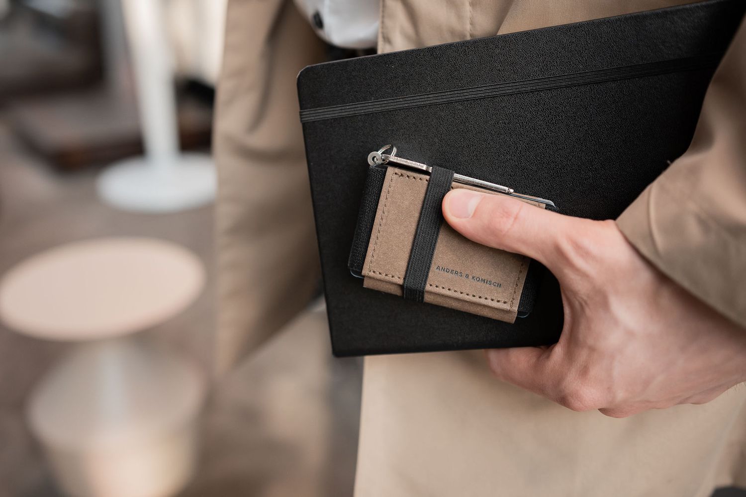 A hand holds a sleek black and brown leather wallet against a blurred background.