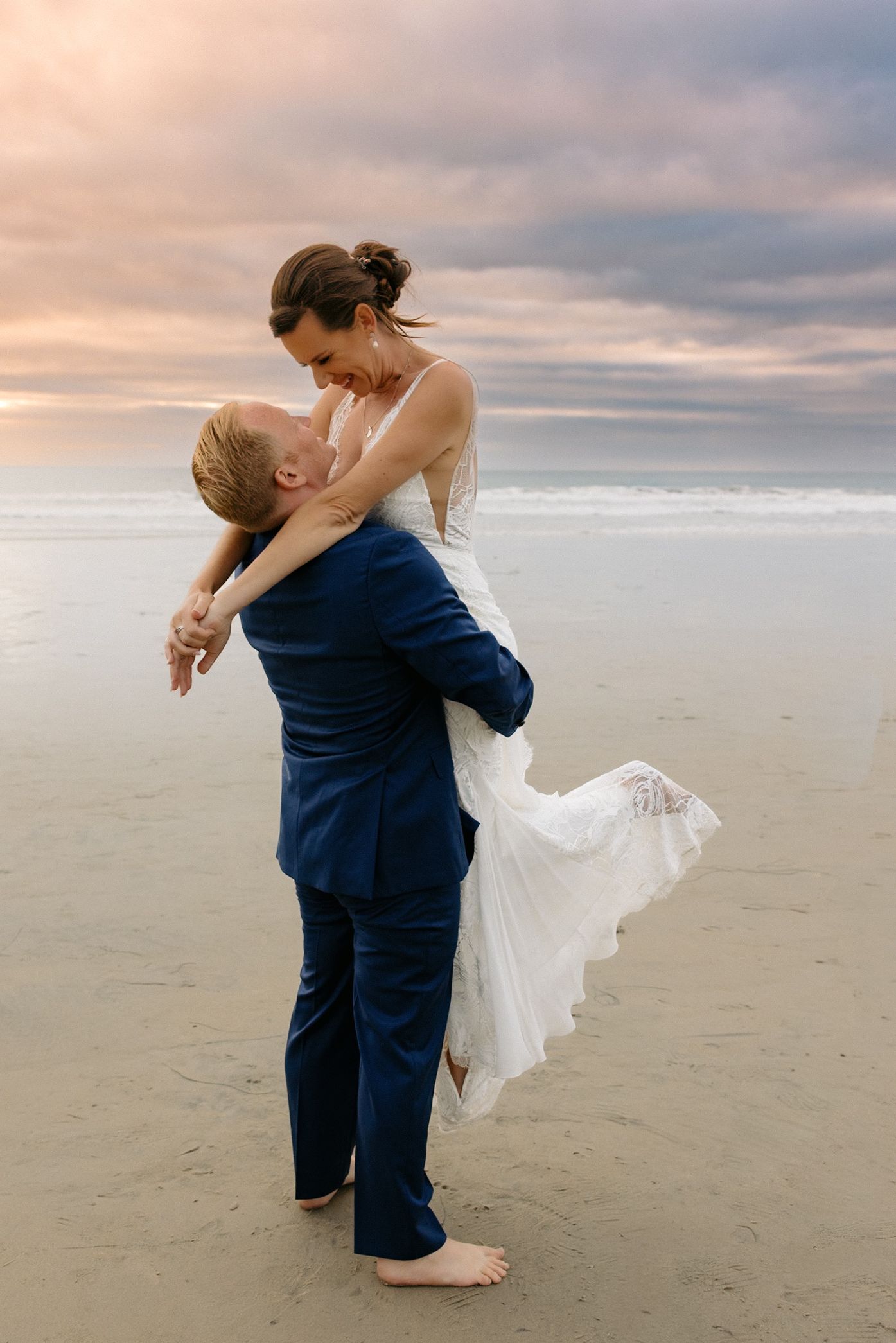 A romantic couple shares an intimate dance moment on a cloudy San Diego beach at sunset.