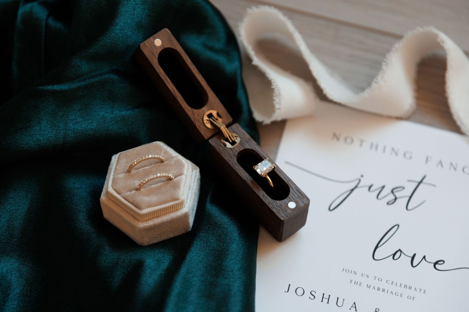Wedding items including a hexagonal ring box and an invitation with 'just love' text on green velvet.