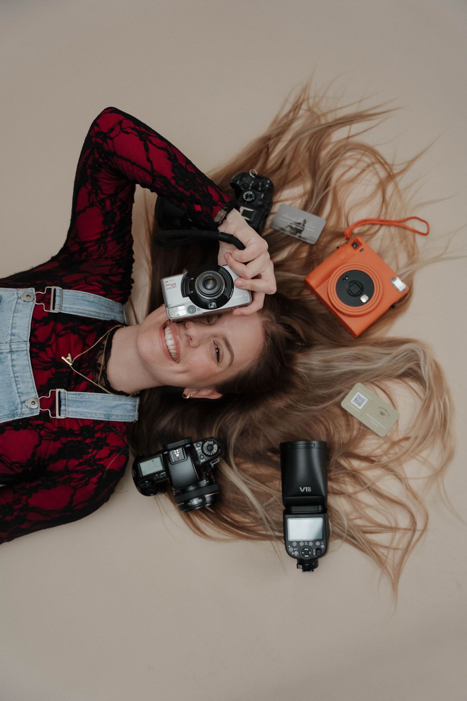 Overhead shot showing camera equipment including lenses, flash units and an orange instant camera arranged around flowing blonde hair.