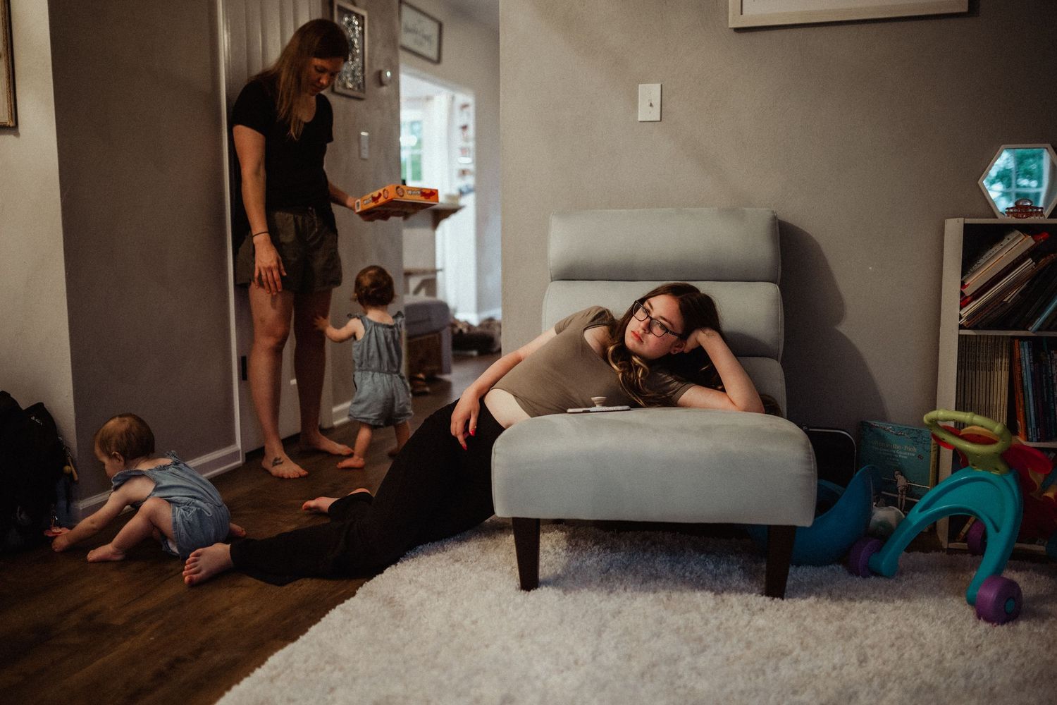 at home family documentary session with teenager draped over a chair in a toddler playroom with twin siblings crowd around the mother