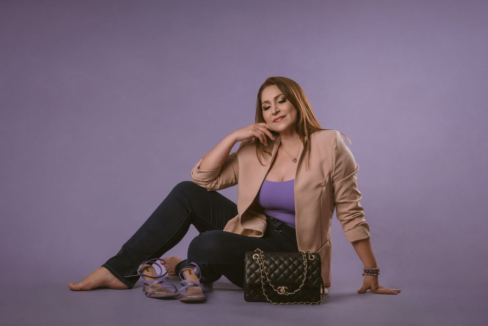 Casual fashion portrait with tan blazer, purple top, and designer bag against lilac background.