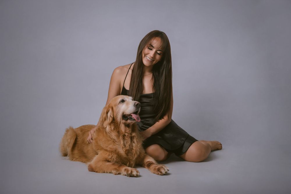 Person in black dress sitting with golden retriever during studio photoshoot.