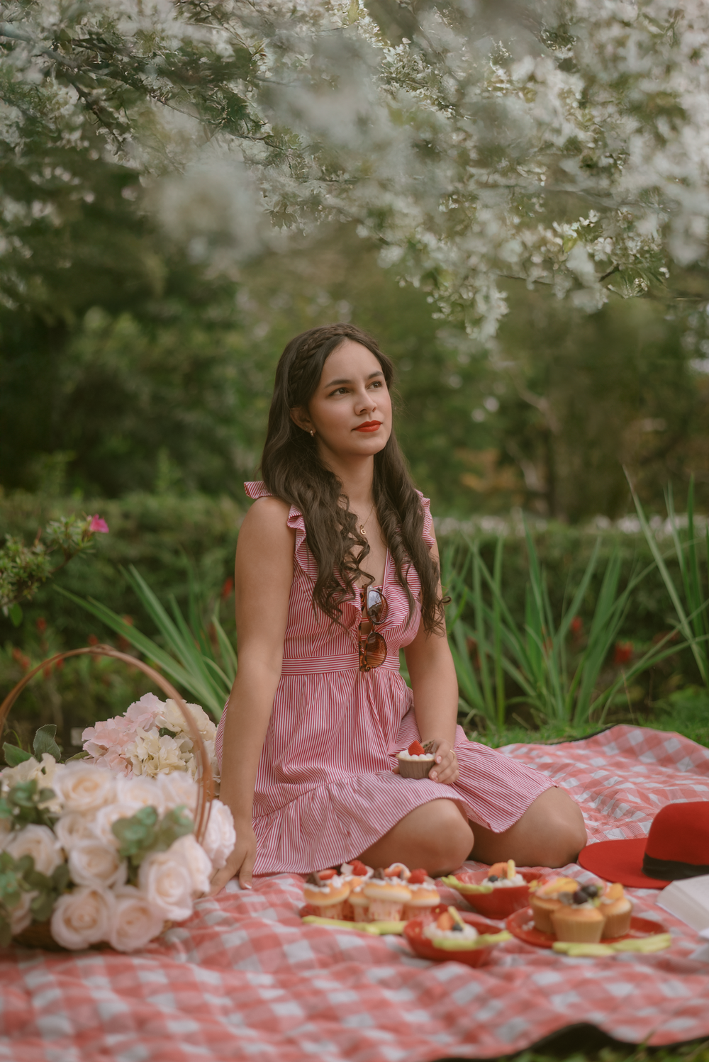 Outdoor spring picnic scene with blooming flowers and treats laid out on checkered blanket.
