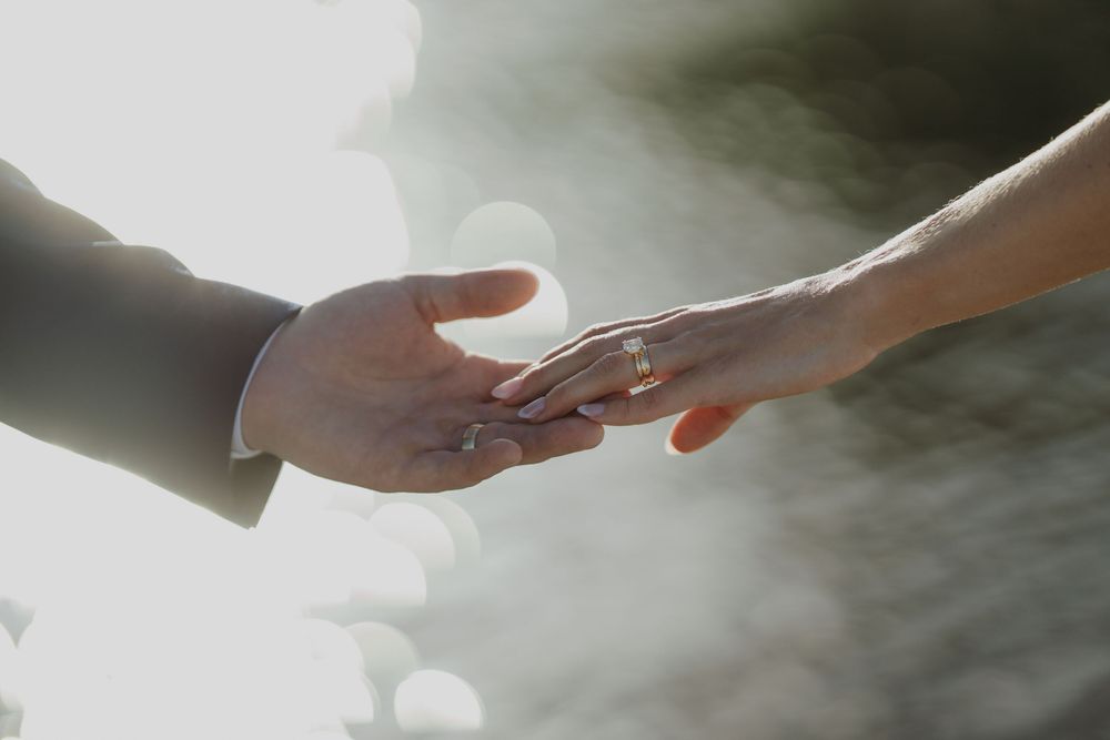 Two hands gently touching, exchanging a wedding ring during a romantic ceremony with soft natural light.