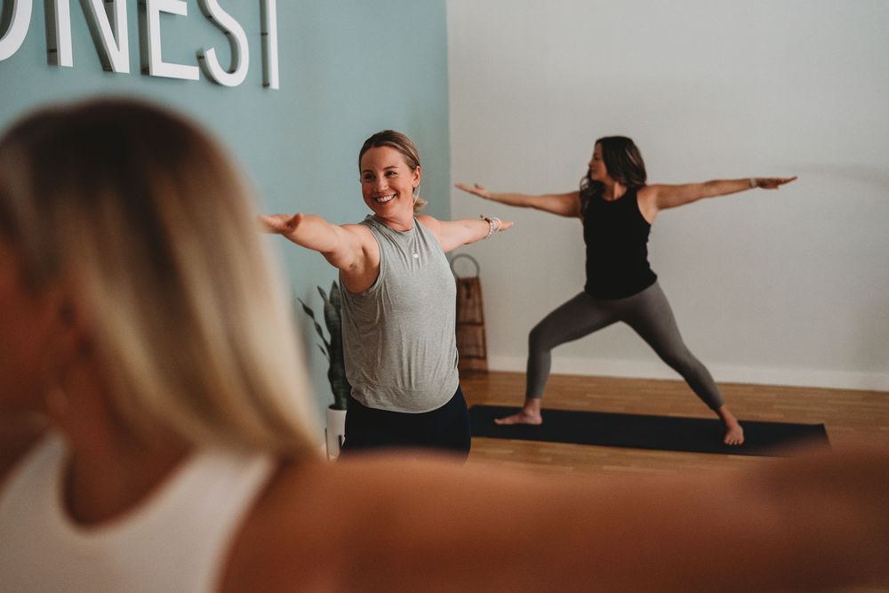 People practicing yoga together in a bright studio space with white walls and wooden floors.