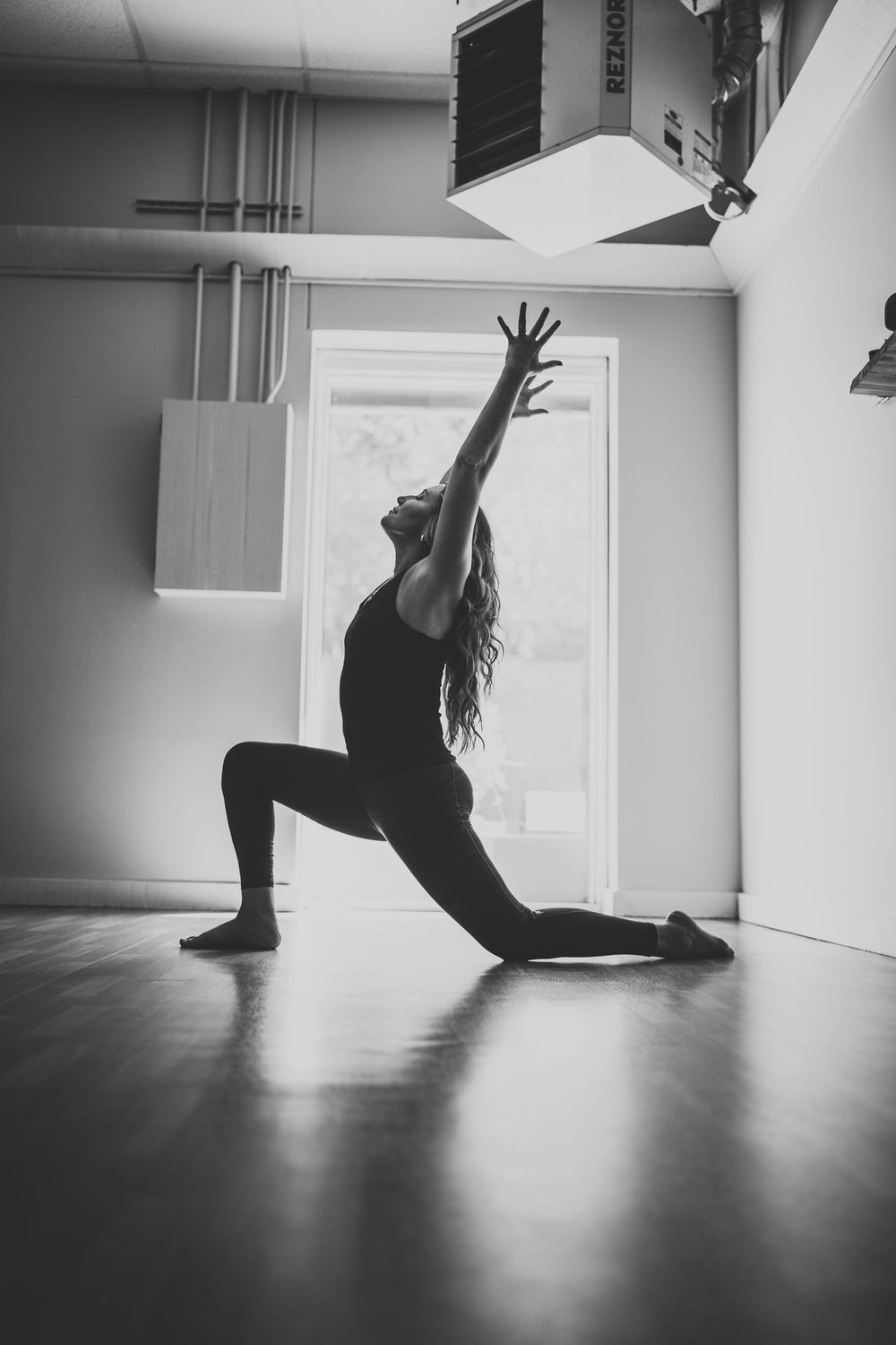 Silhouette of a dancer in a dramatic lunging pose with arm raised reaching upward in a dance studio.