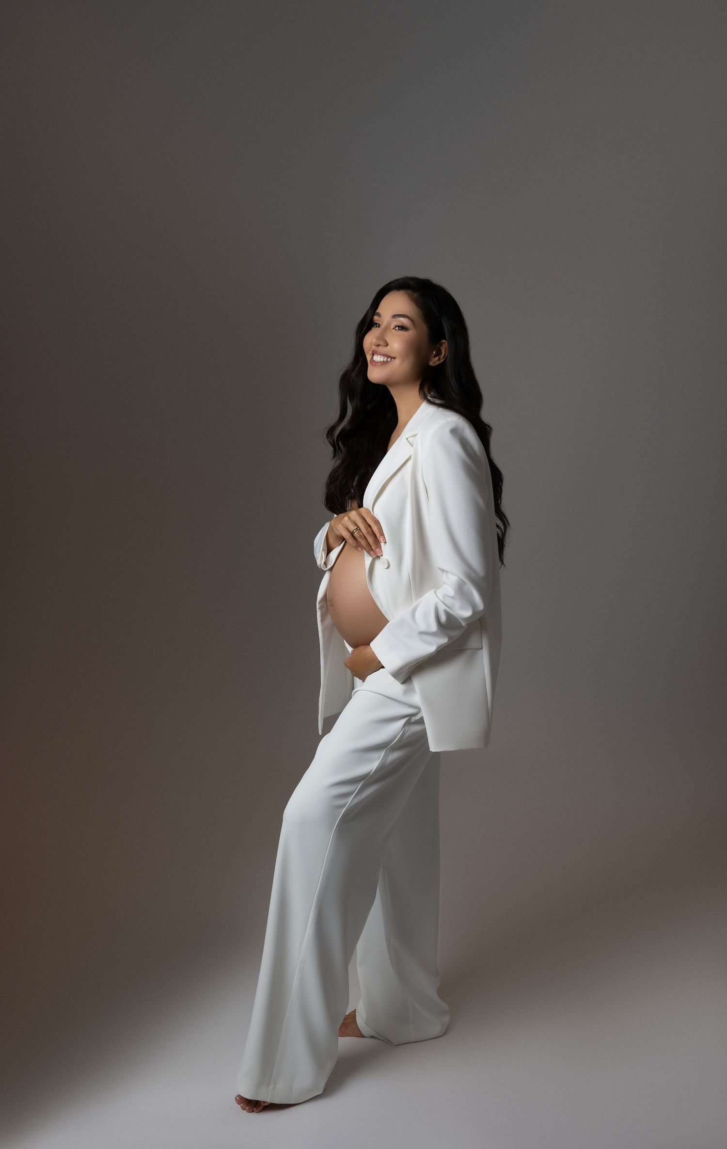 An artistic maternity photo series shows a person in a flowing white dress against a grey studio background.
