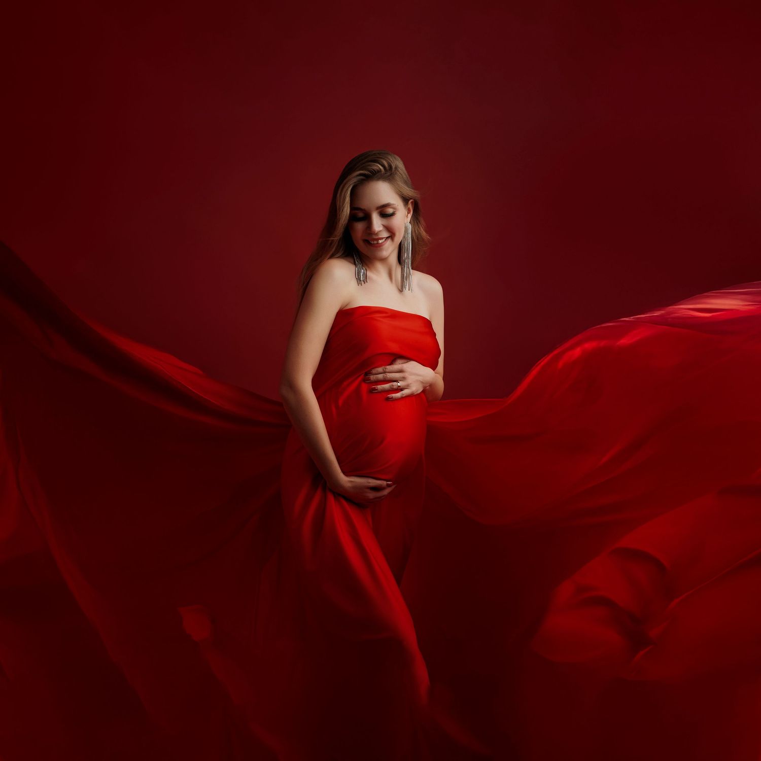 Artistic maternity photo with billowing red fabric in a dark studio setting.