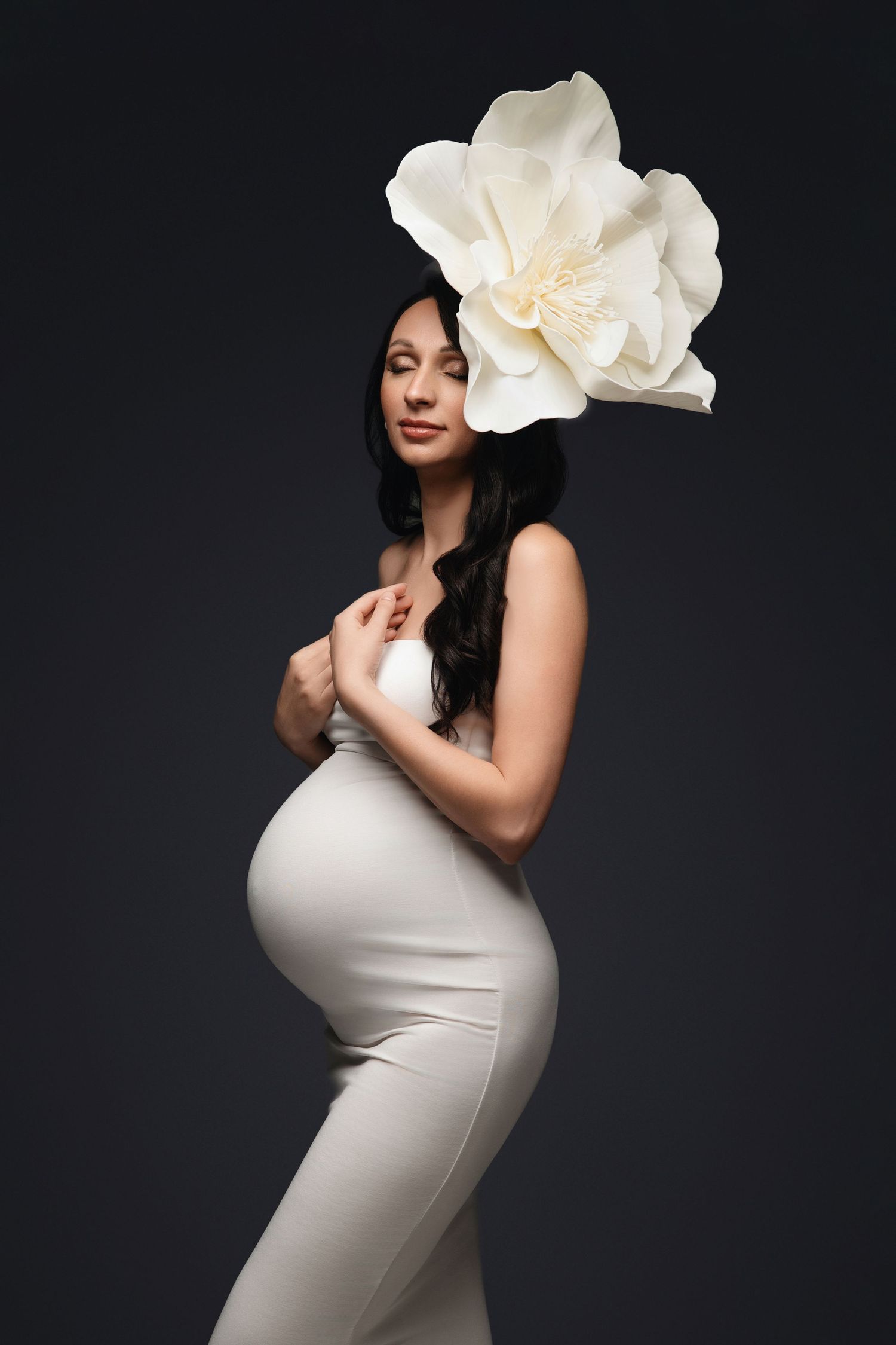 Maternity portrait with large white flower accent against dark background.